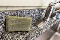 A sparkly gold dishwashing sponge from Hawkins New York next to a kitchen sink