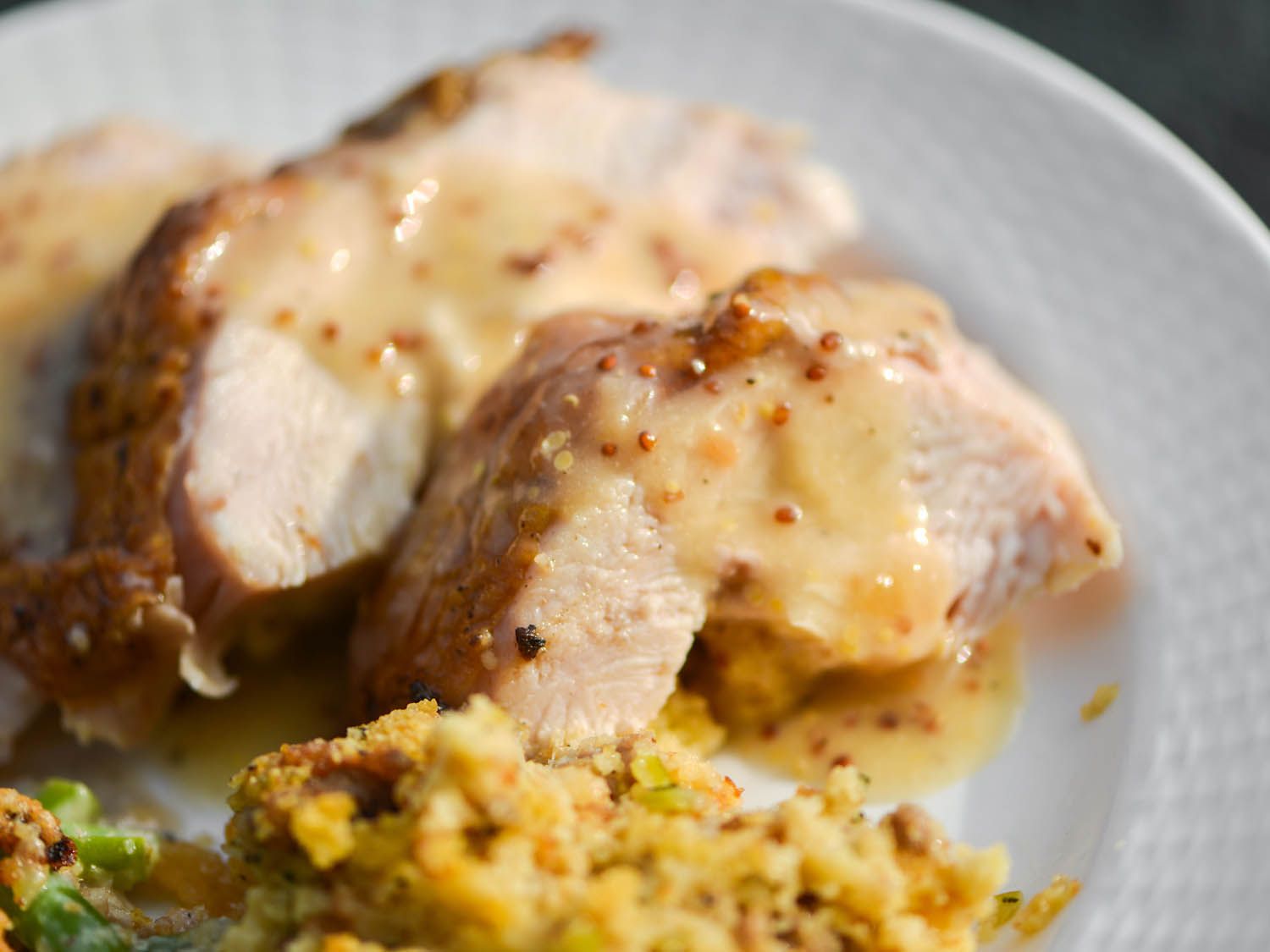 Smoked turkey breast slices topped with white white and mustard gravy, all on a white plate with cornbread dressing on the side.