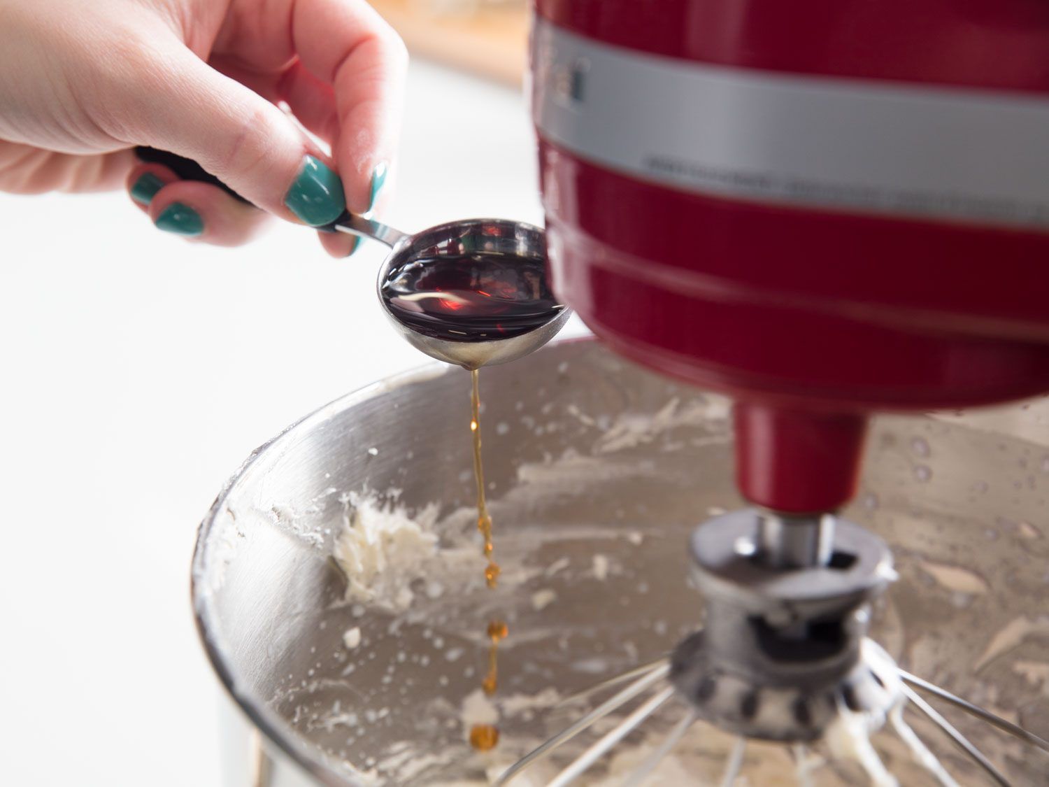 Adding vanilla extract to ermine frosting in the bowl of a stand mixer.