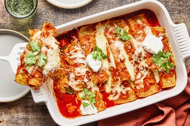 Freshly baked sweet potato enchiladas topped with melted cheese cilantro and dollops of cream served in a casserole dish