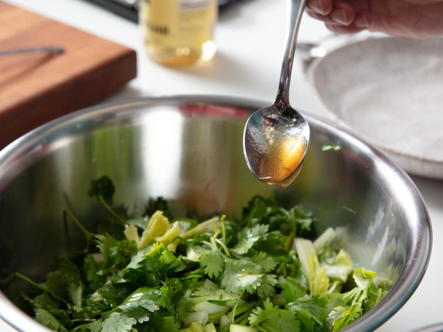 A spoon drizzling dressing over tiger salad in a bowl.