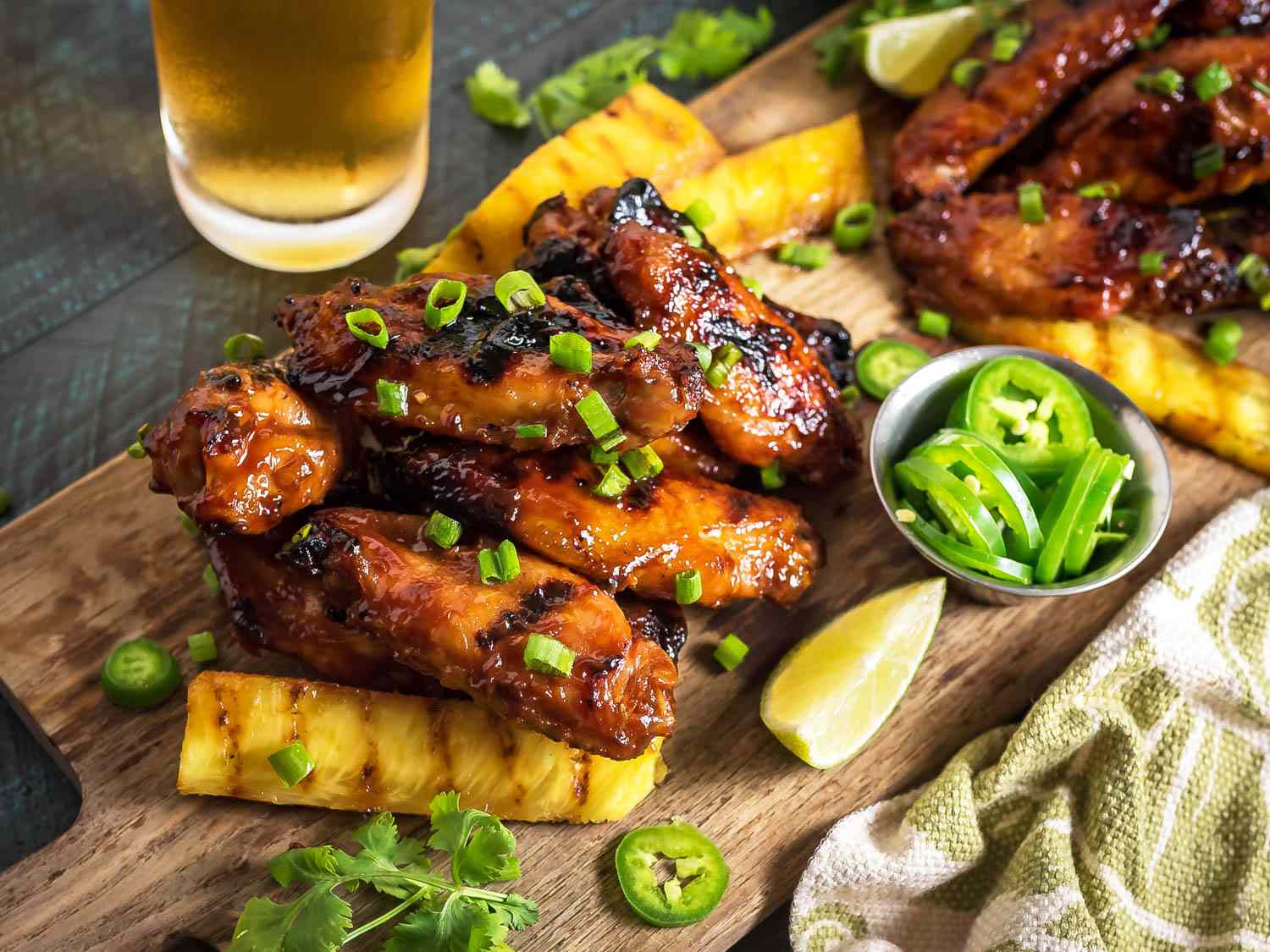 A wooden cutting board covered in grilled Hawaiian-style wings with grilled pineapple.