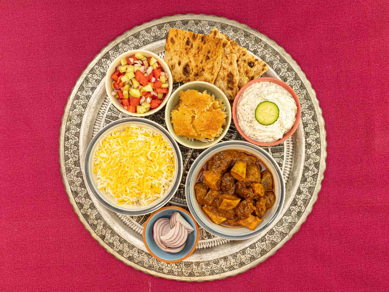 A tray with various dishes including khoreshebeh rice flatbread and side dishes such as yogurt and pickled vegetables