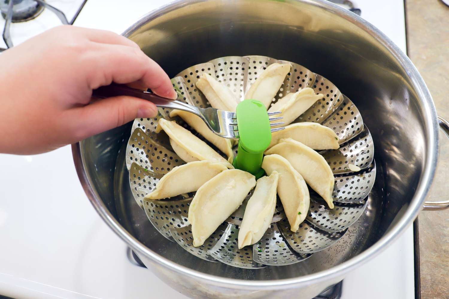 A person lifting a steamer basket cooking dumplings out of a pot.