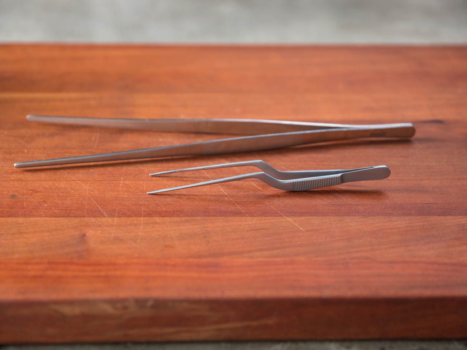 two pairs of kitchen tweezers on a wooden surface