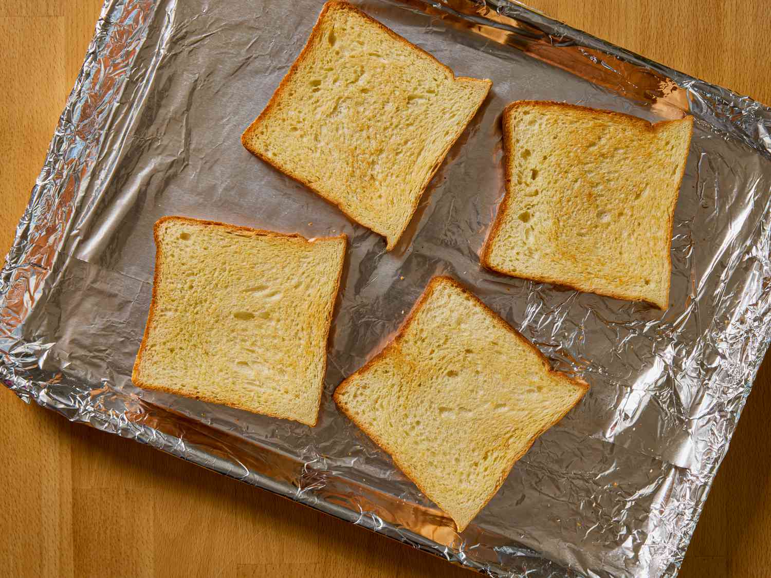 Four slices of toasted bread arranged on a foil-lined baking sheet