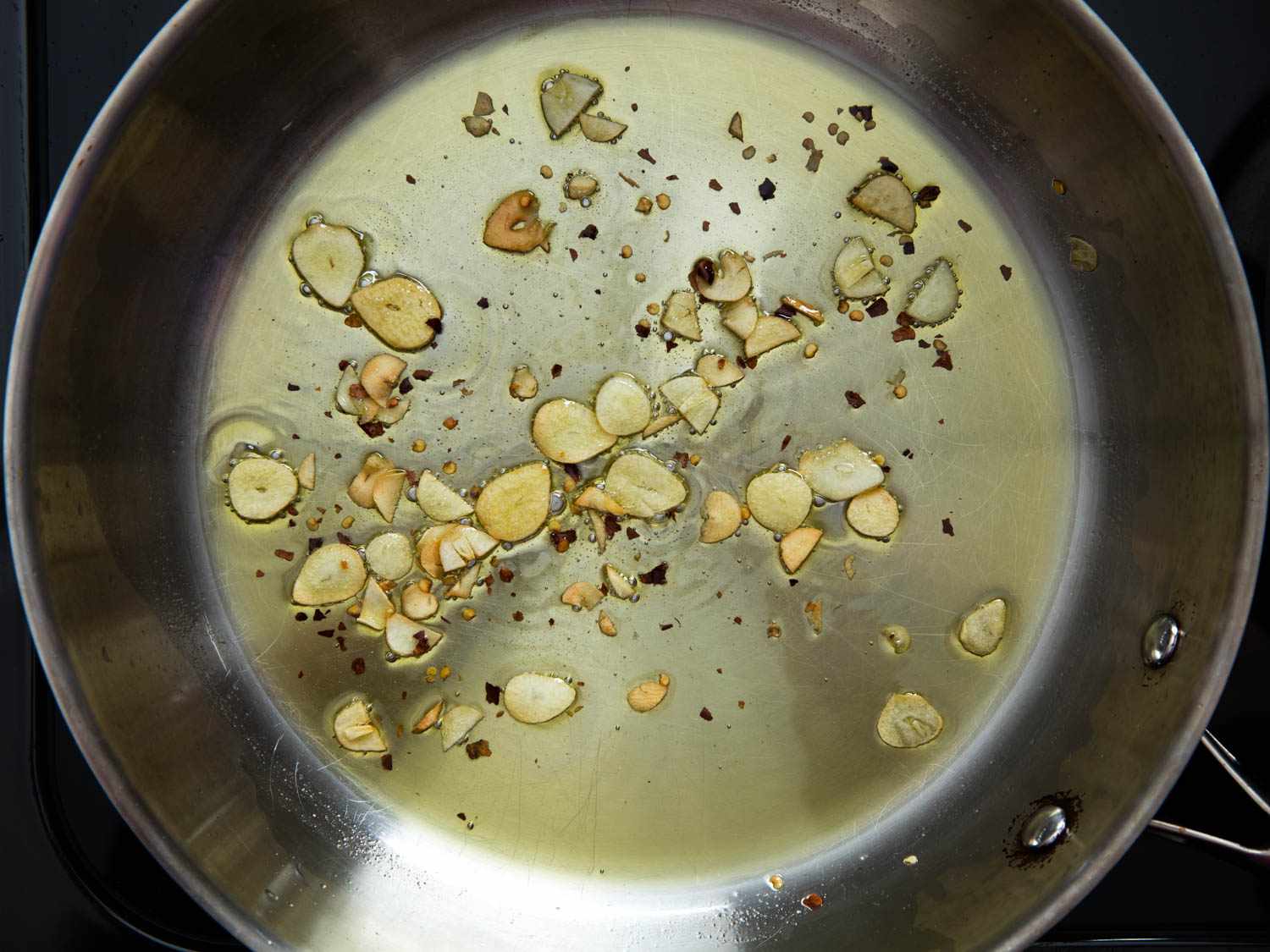 Irregularly cut garlic cooks in olive oil. Smaller pieces of garlic are blackening.