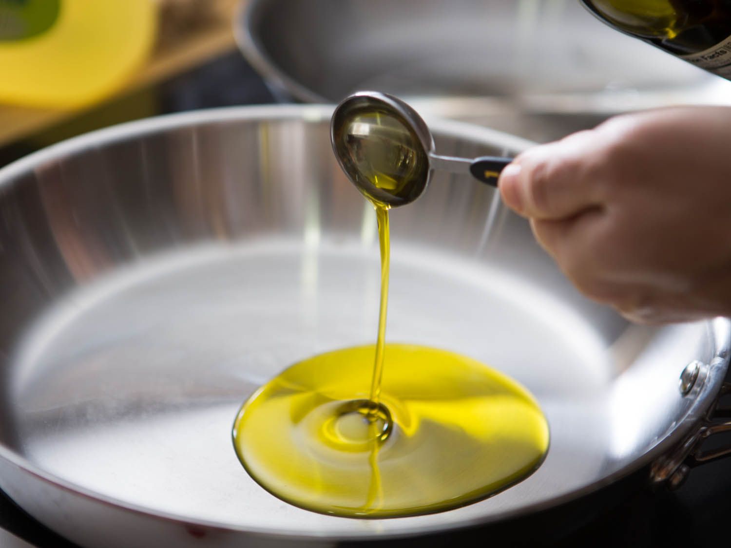 Pouring a tablespoon of olive oil into a stainless steel skillet.