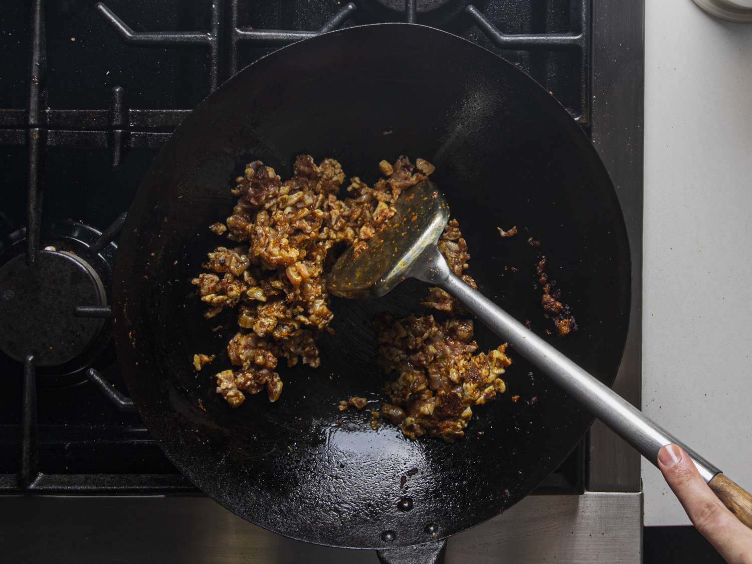 A metal spatula moving chicken around in a wok. 
