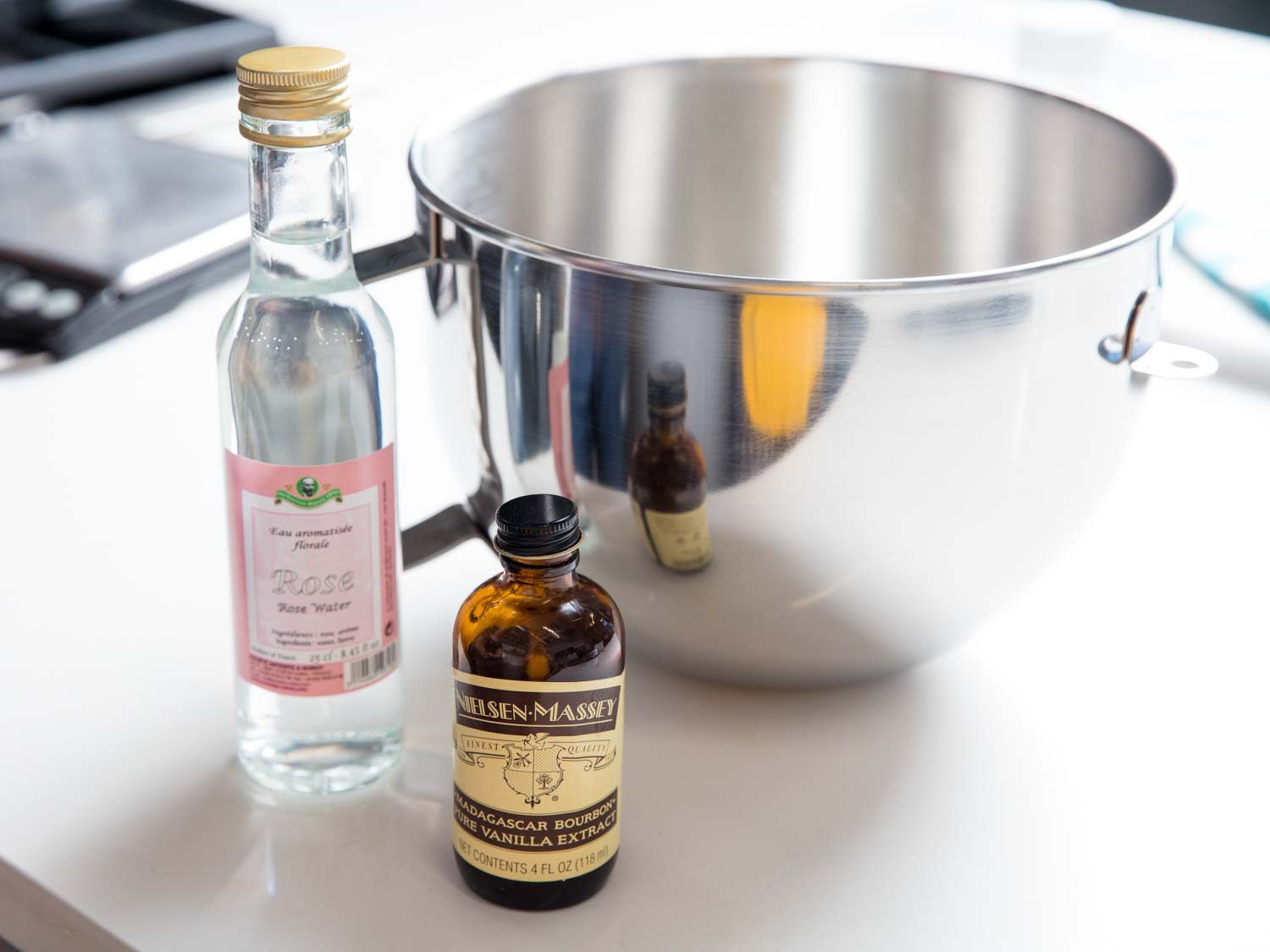 Bottles of rose water and vanilla extract next to a mixer bowl.
