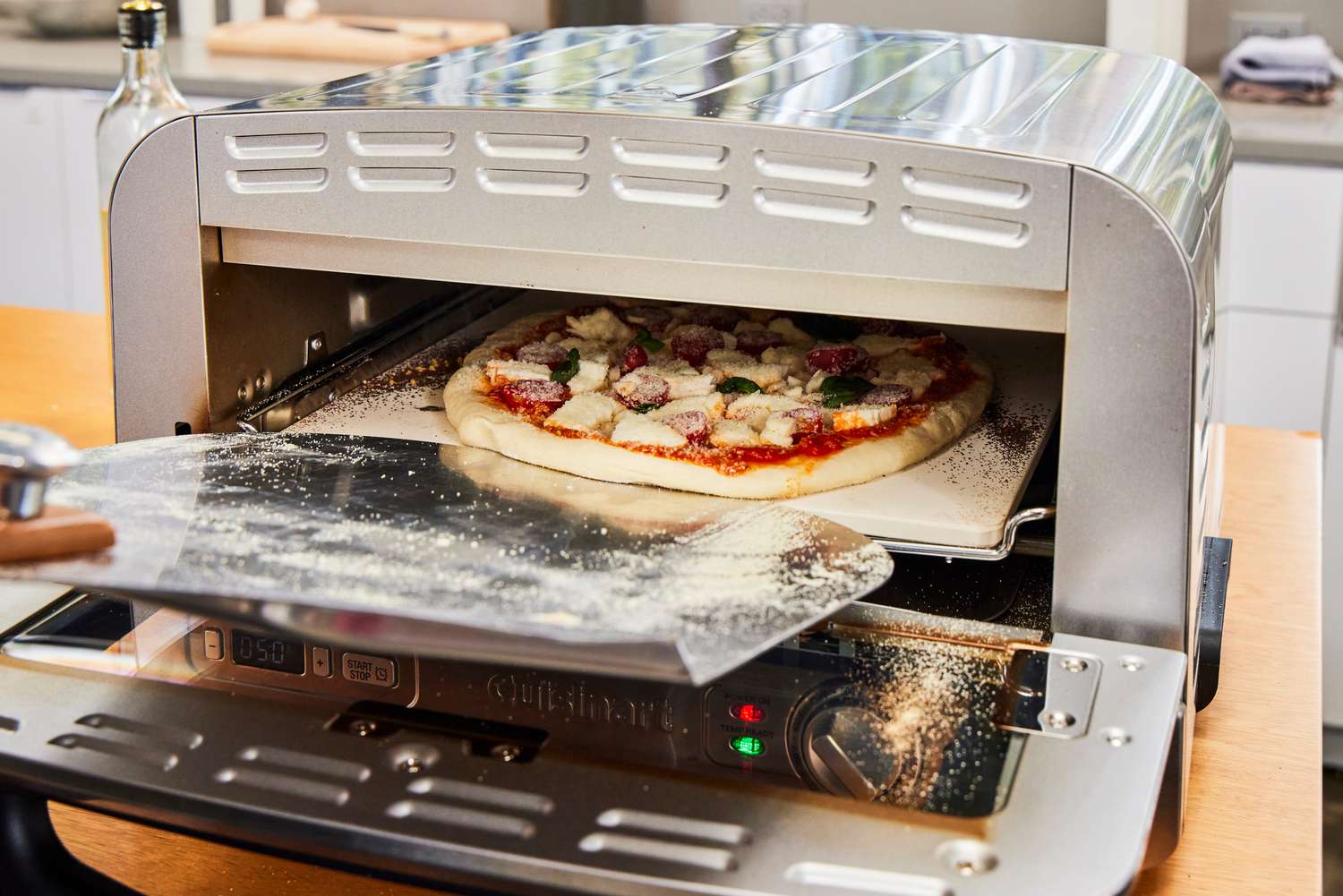 A person places a pizza into the Cuisinart CPZ-120 Stainless Steel Indoor Pizza Oven