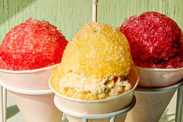 Three snow cones in paper cups one yellow in the center and red ones on the sides