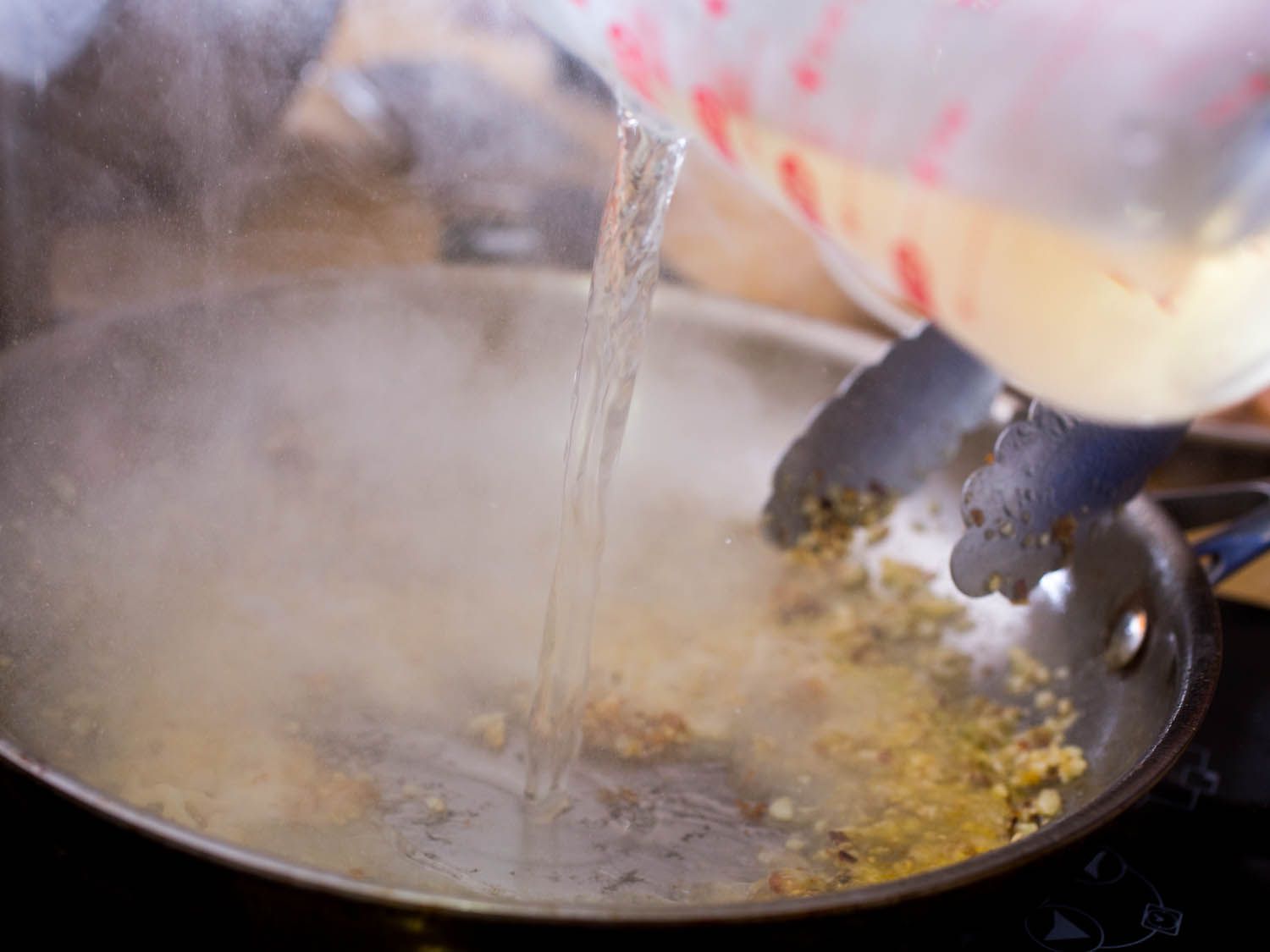 Pouring vermouth from a glass measuring cup into a skillet of garlic butter sauce for shrimp scampi.