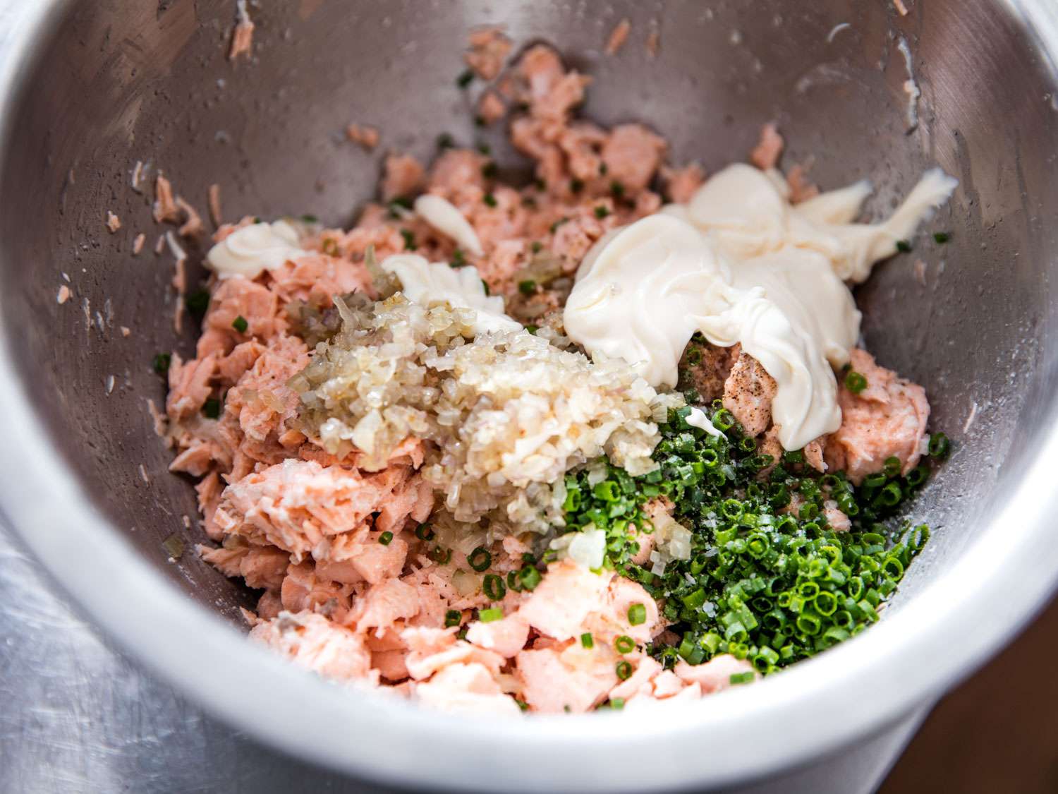 A bowl of shredded salmon, mayo, cooked shallots and chives for rillettes.