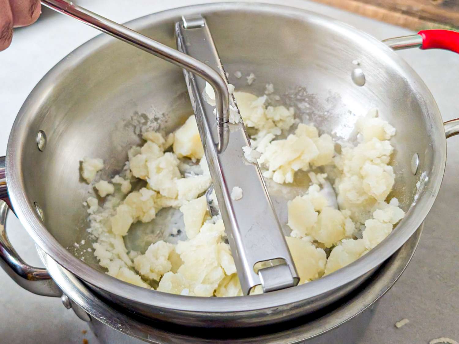 Potatoes being mashed with a ricer in a metal pot