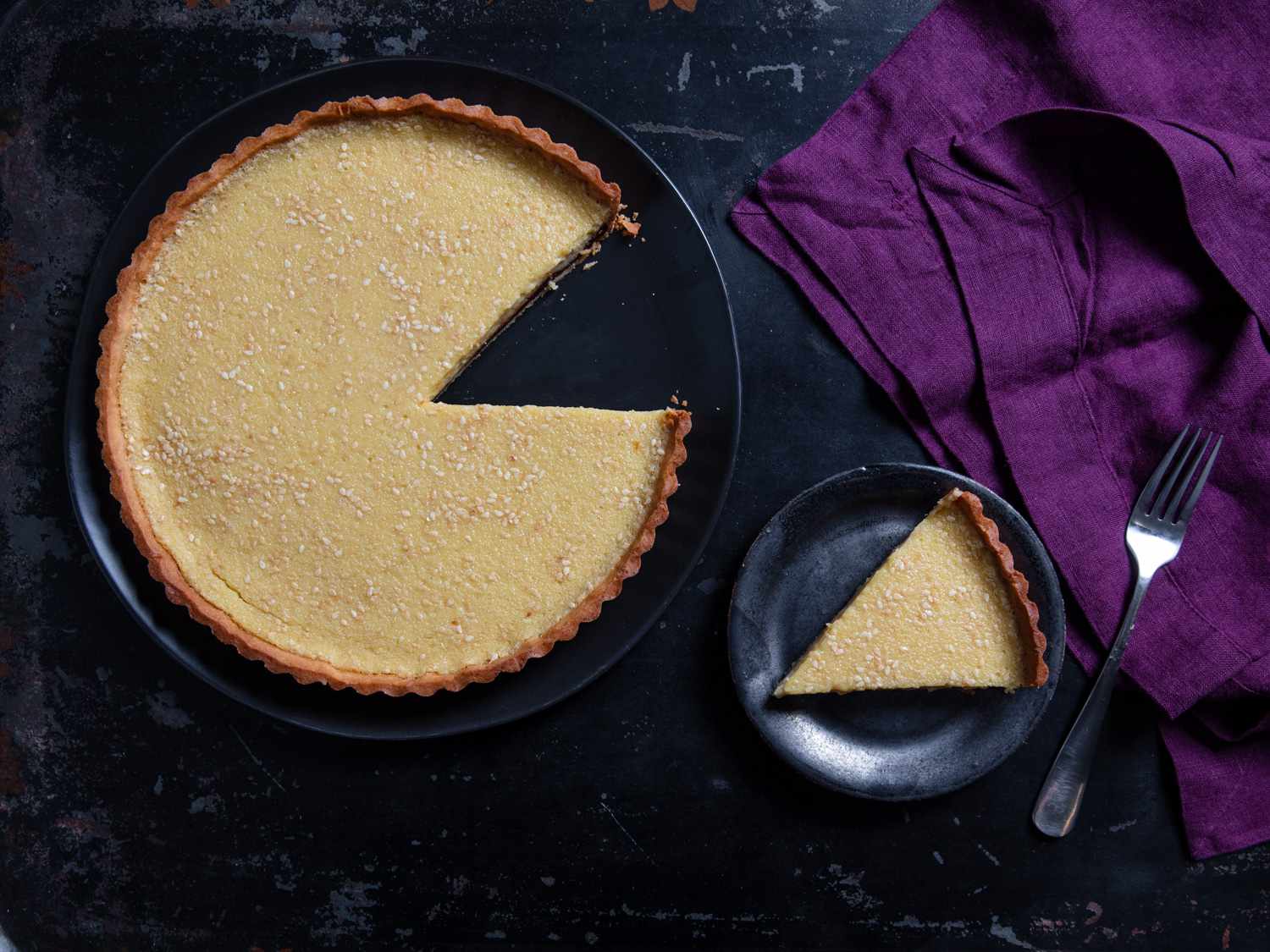 an overhead shot of a slice of toasted white sesame tart with bittersweet chocolate ganache next to the full tart