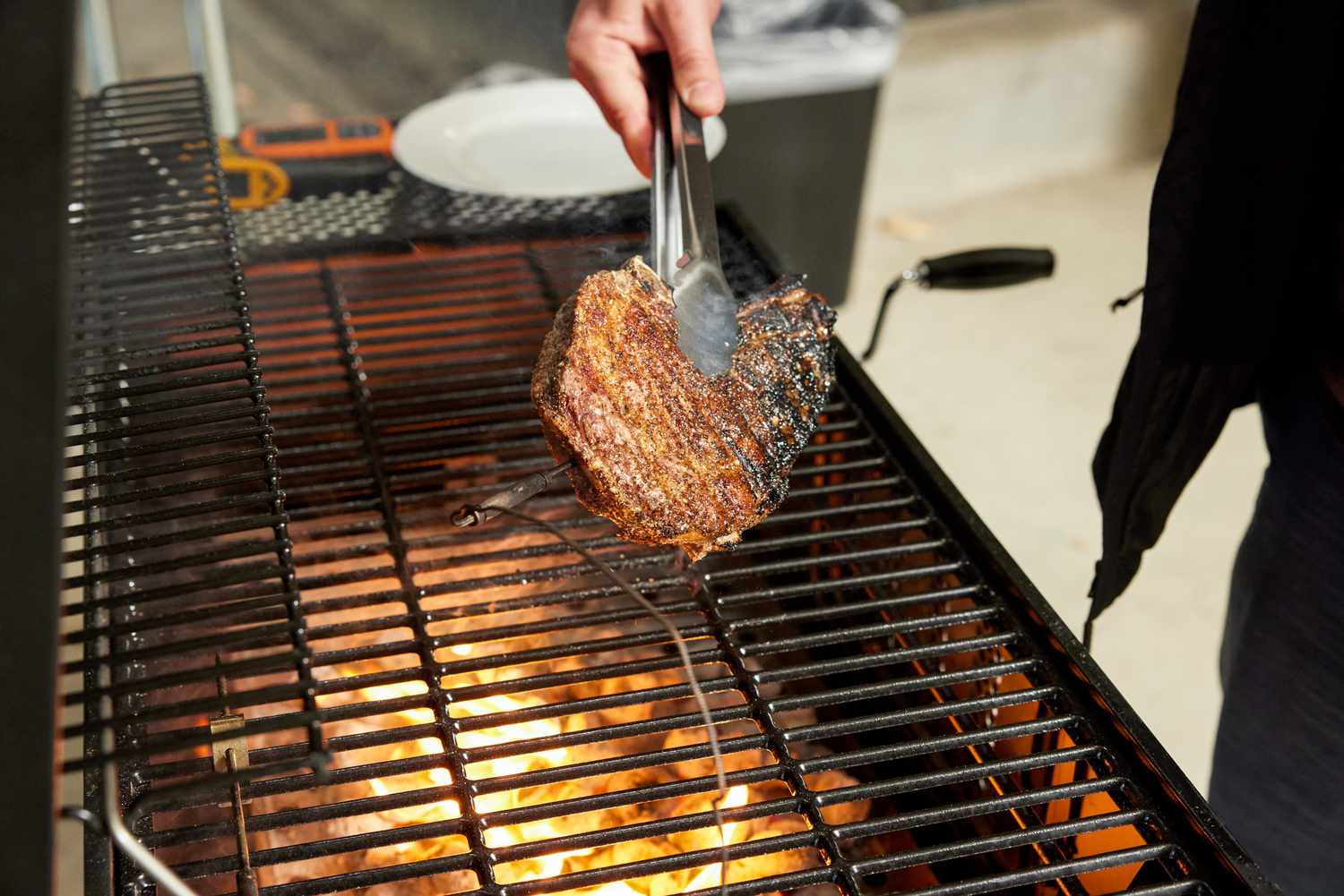 A steak is held with tongs over a hot charcoal grill
