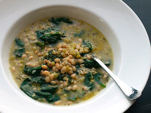 Closeup of hearty white bean and spinach soup with rosemary and garlic in a wide white bowl.