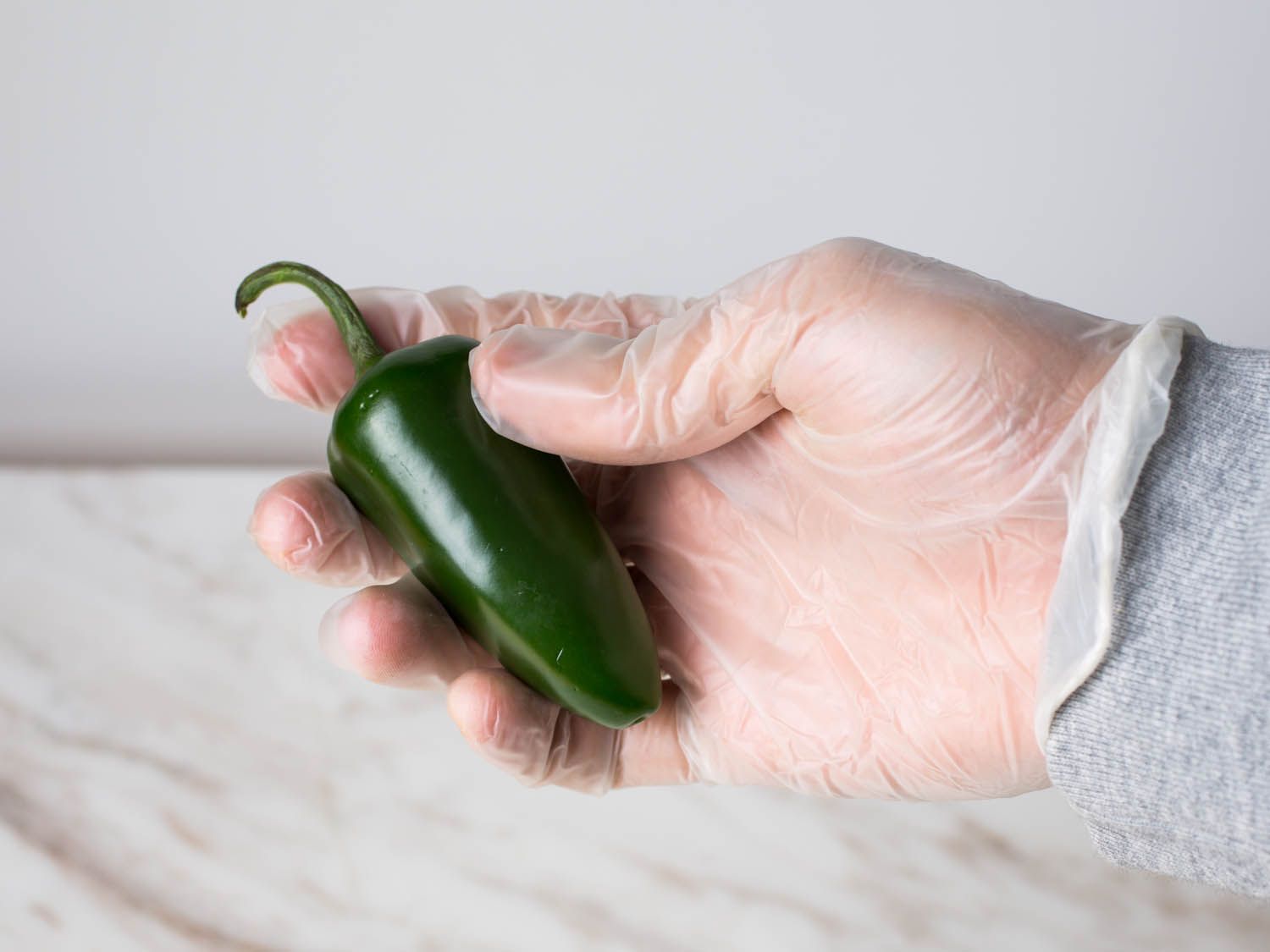 A gloved hand holds a whole fresh jalapeño.