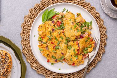 A plate of a prepared Nigerianstyle omelet garnished with herbs accompanied by a bagel and a cup of tea on a woven mat