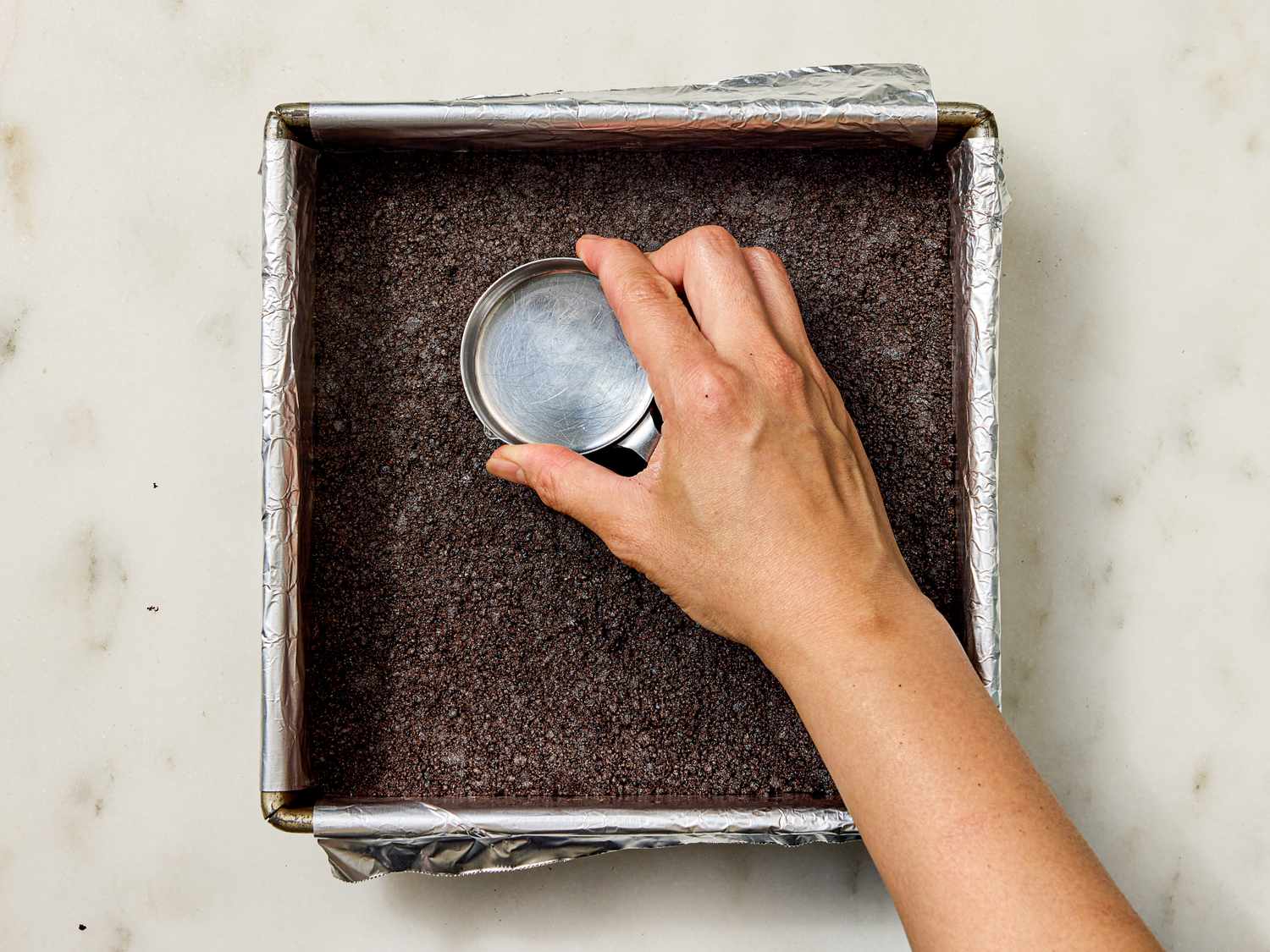 Pressing a layer of crumbs into a baking pan with the bottom of a cup