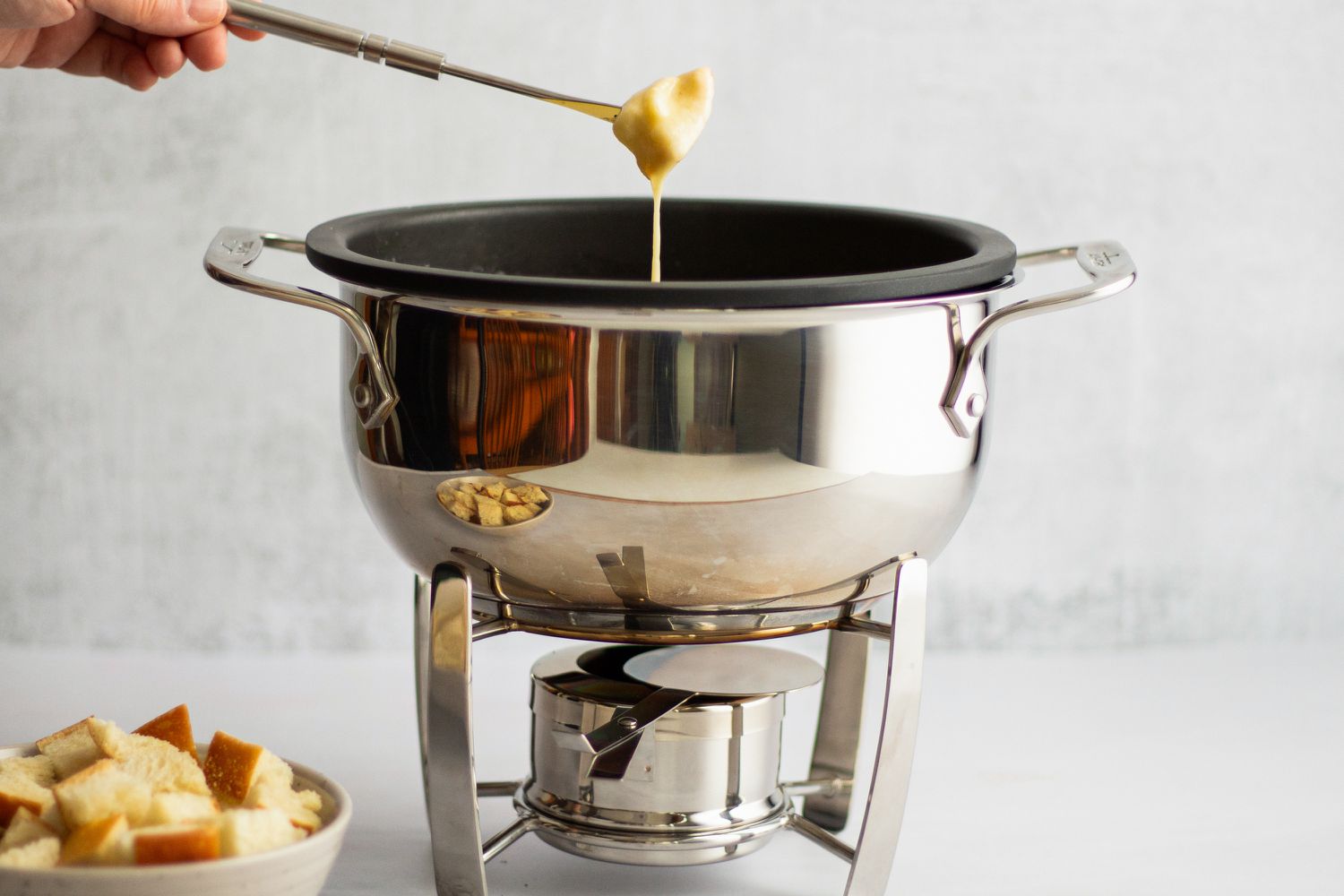 A person dipping a chunk of bread into cheese fondue in a fondue pot.