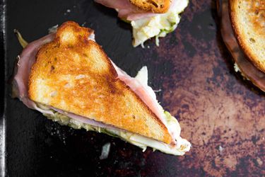 Overhead view of a halved Grilled Mozzarella Sandwich With Mortadella, Pesto, and Artichokes.