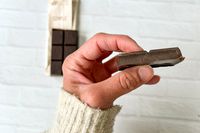 A hand holding a piece of Hu Simple Dark Chocolate