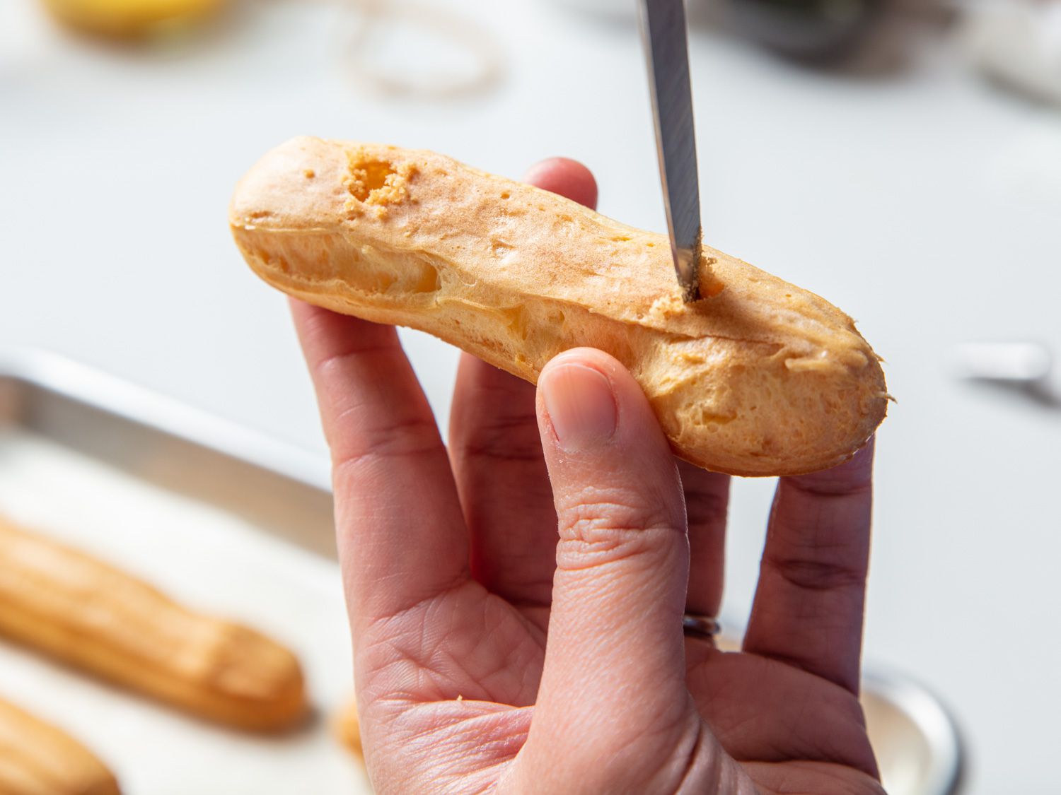 A knife poking two holes into the baked éclair for adding filling.