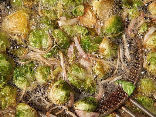 A metal spider scooping out golden-brown fried Brussels sprouts and shallots.