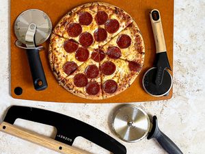 Pepperoni pizza on a board surrounded by pizza cutters