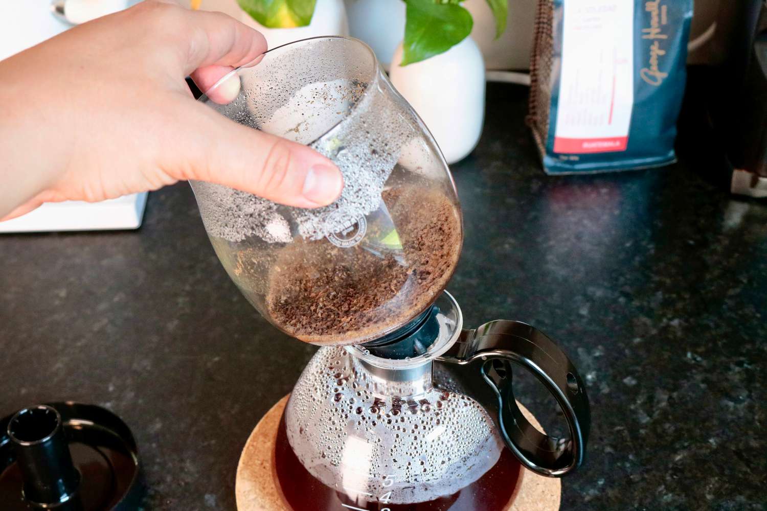 a hand removing the top portion of a siphon brewer from the bottom
