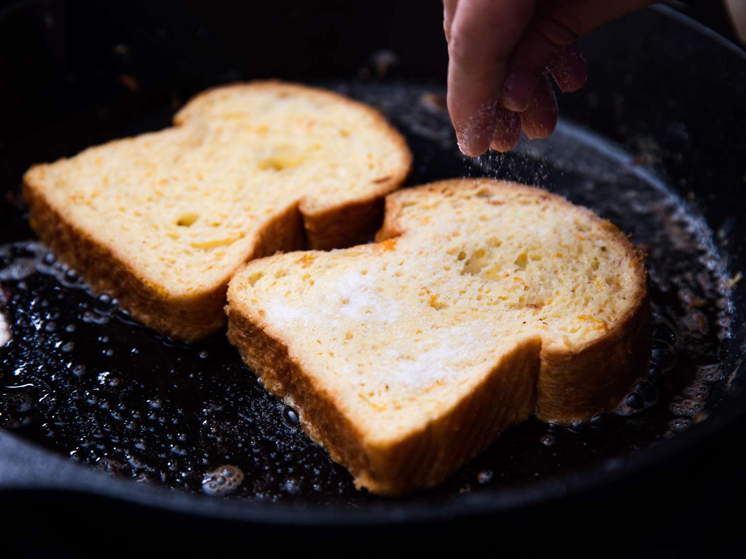The prepared challah slices are cooked in a cast iron skillet and sprinkled with sugar.