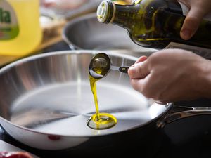 Pouring a tablespoon of olive oil in a skillet to test if it's okay to use olive oil for high heat cooking.
