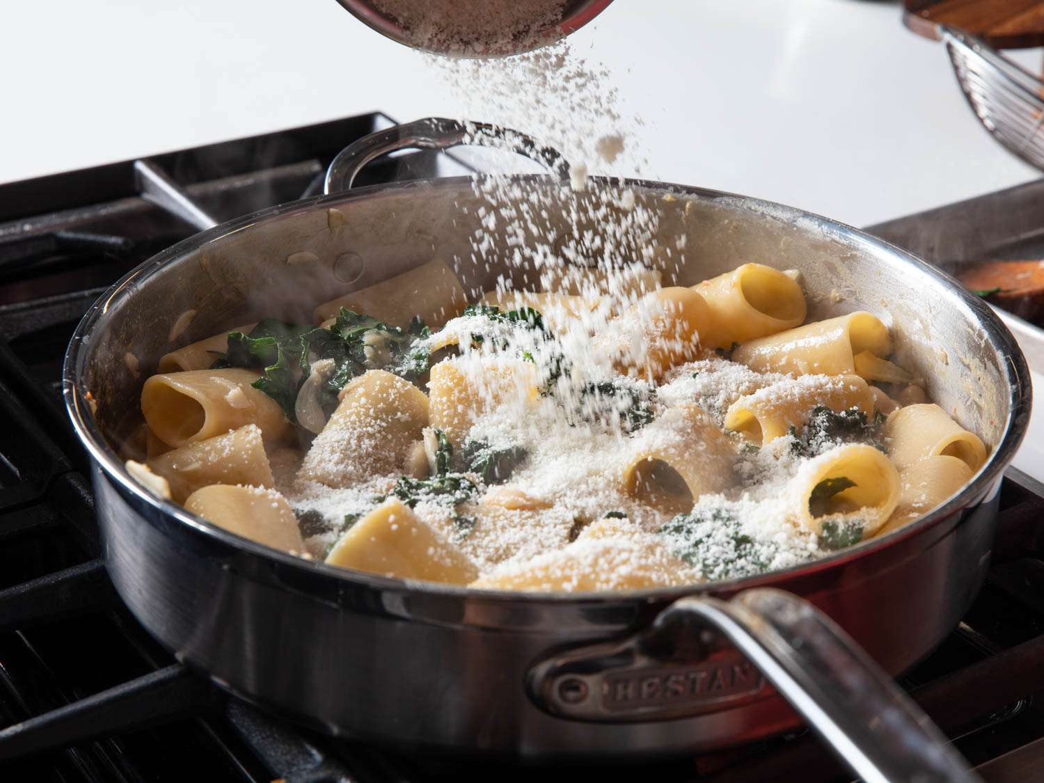 Adding cheese to a pan of rigatoni with bean sauce