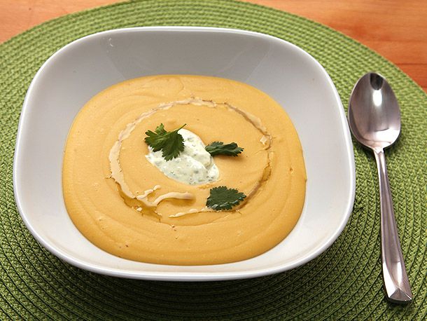 Red lentil soup, served in a square-ish bowl and garnished with curry yogurt, several cilantro leaves, and a drizzle of olive oil.