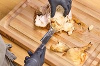 Gloved hands carving a roasted chicken on a John Boos Reversible Maple Wood Cutting Board with Juice Groove