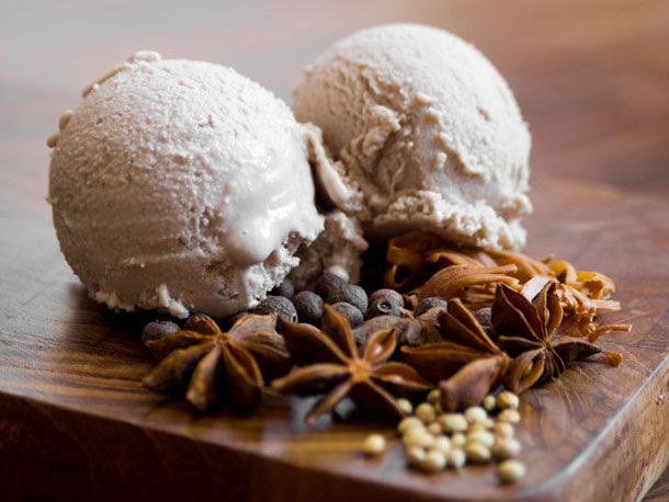 Two scoops of mulled wine ice cream displayed with whole spices: star anise allspice berries, coriander, mace.