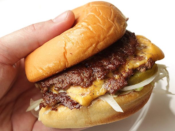 Side view of hand holding a double-stacked smash cheeseburger