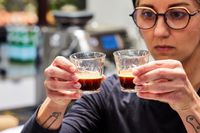 A person holding up two glass espresso cups with espresso inside 