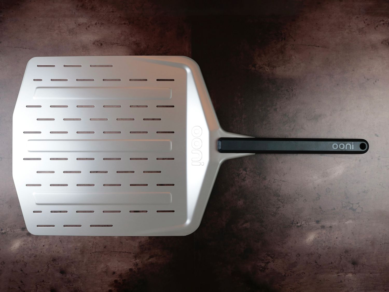 A perforated metal pizza peel on a dark background