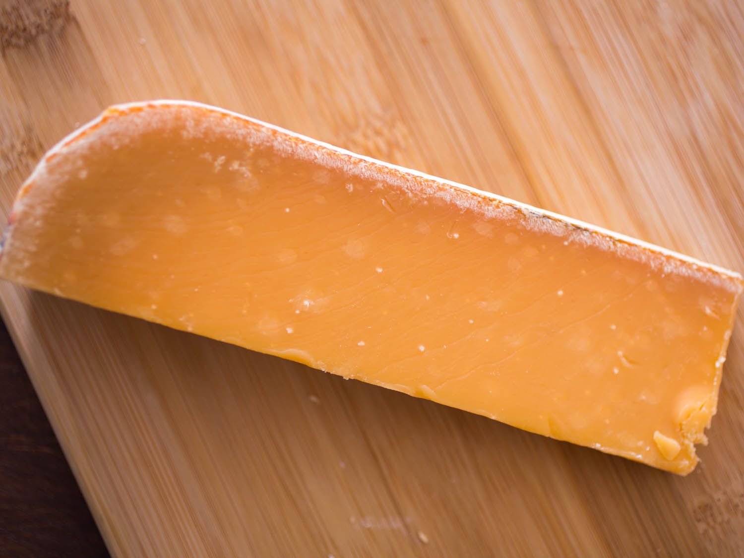 A wedge of orange aged Gouda on a wooden board.
