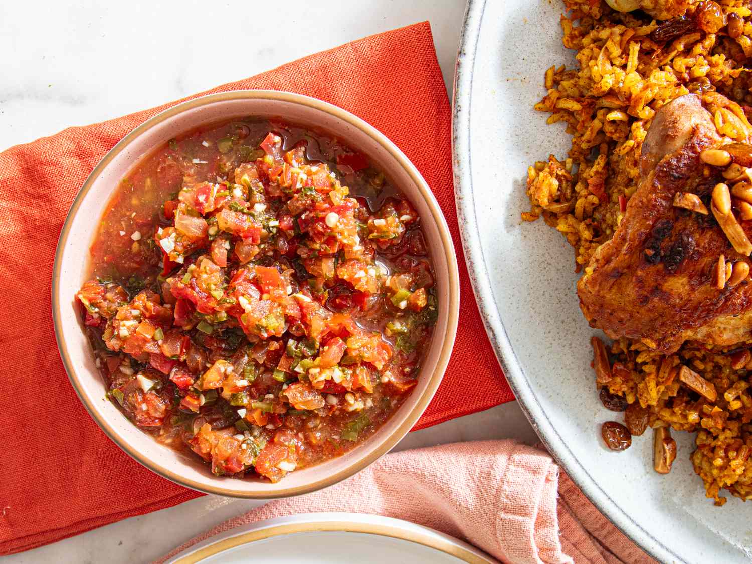 A bowl of salsa next to a plate of rice and chicken