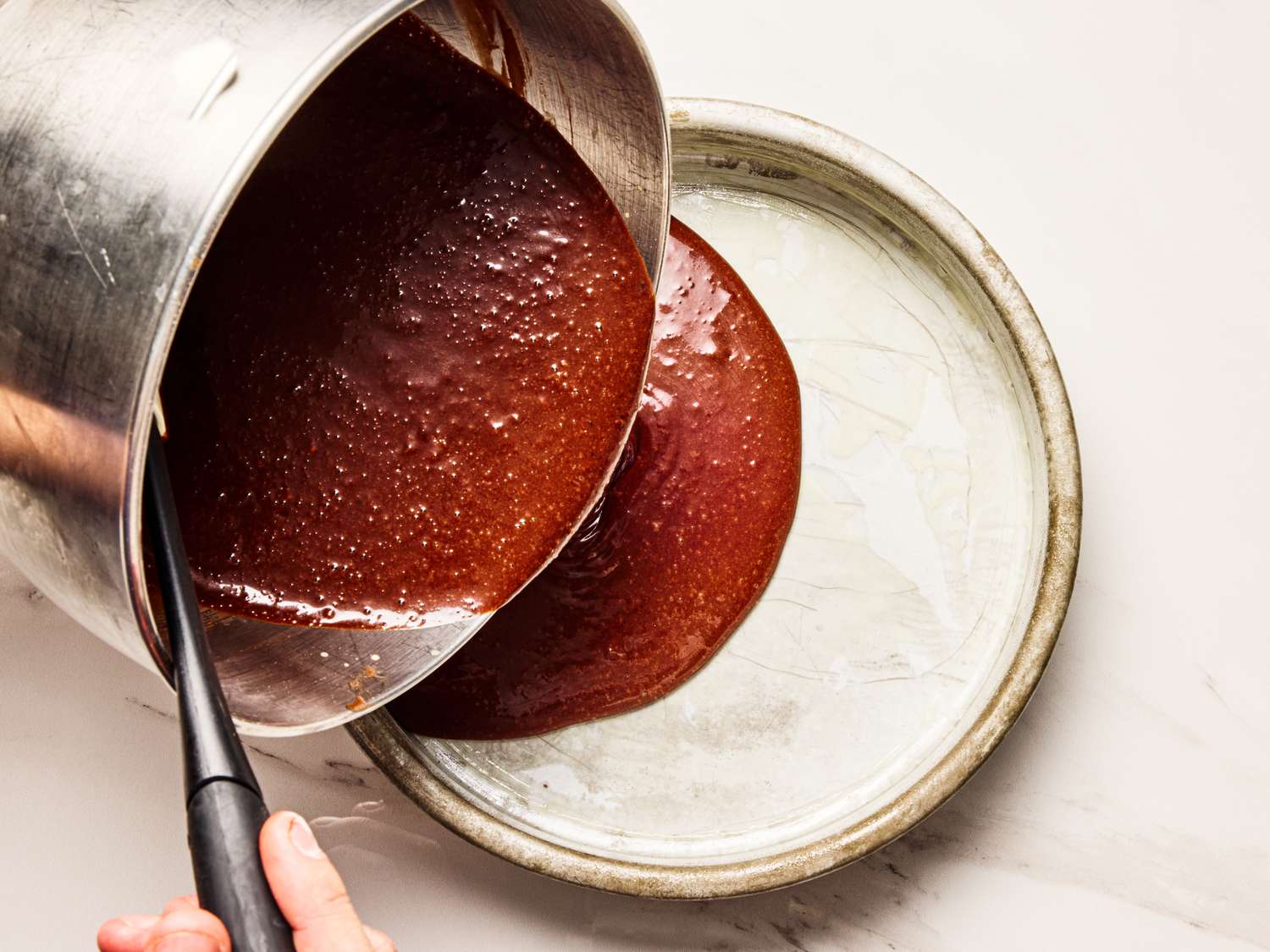 Pouring chocolate batter into a round cake pan