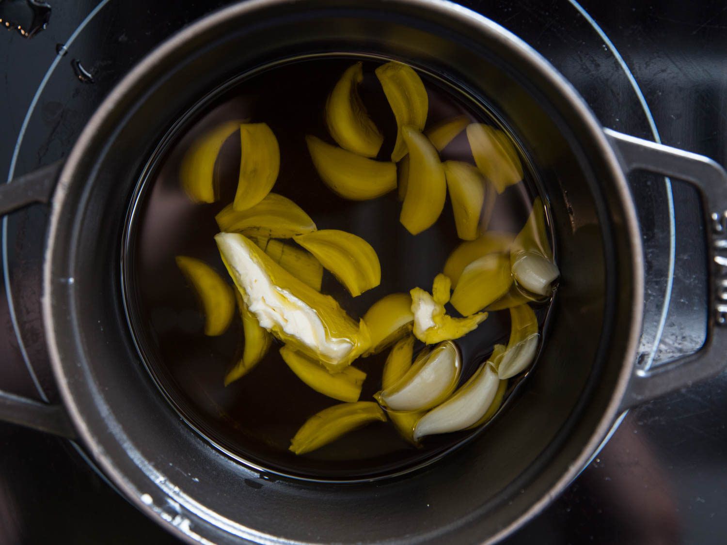 Overhead shot of cloves of garlic floating in a pot of olive oil.