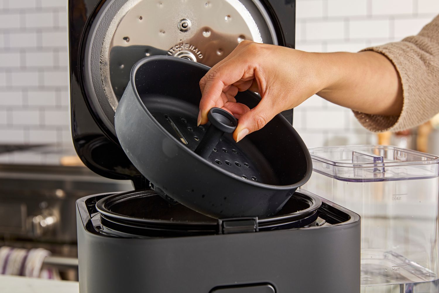 A person lifting the steamer basket out of the KitchenAid rice cooker.