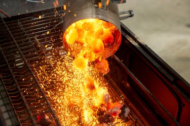 Charcoal being poured into a charcoal grill from a chimney starter.