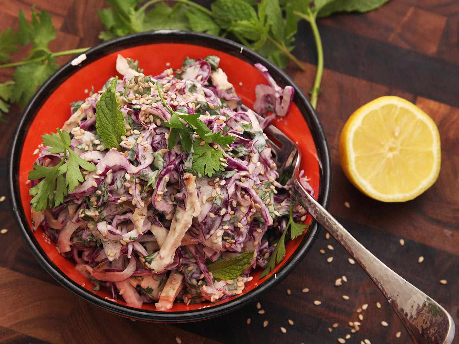 Salad of leftover grilled chicken and red cabbage with tahini dressing in a bowl on a wooden surface, next to a lemon half