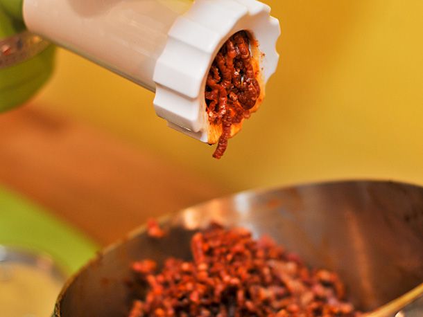 Sausage slowly emerging from the the grinder. A mixing bowl lies underneath.