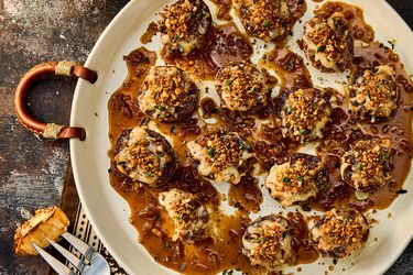 Plate of baked appetizers topped with breadcrumbs and a fork with a slice of bread on a table
